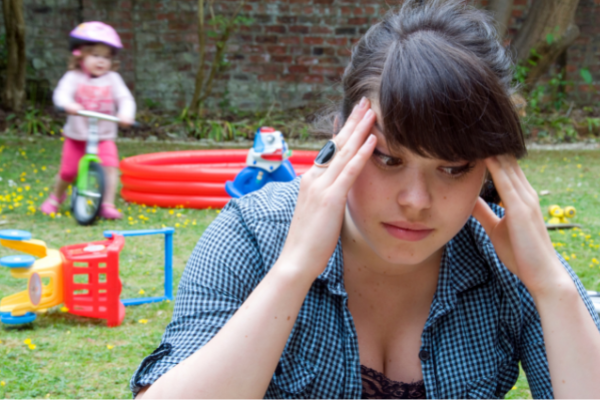 A mom holds her head in frustration while her kids play noisily in the background. The Hacky Homemaker is expressly designed to help parents who feel like this!