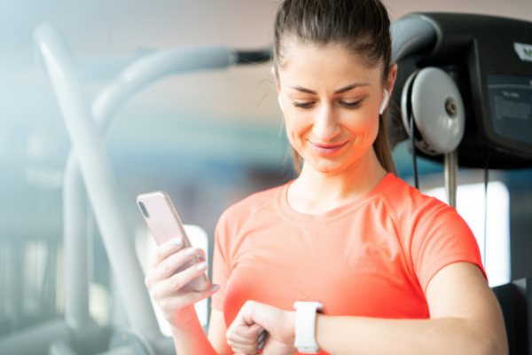 At the gym, a woman pauses from her workout to check her progress on her watch and phone - The Hacky Homemaker - How to get paid for drinking water, eating food, and taking steps every day