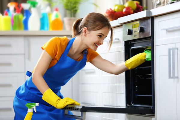 A woman wearing rubber gloves is smiling while she scrubs the inside of an oven - Oven Cleaning Hacks - The Hacky Homemaker