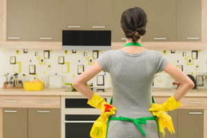 A woman stands in the kitchen with hands on hips, assessing the oven's cleanliness or lack thereof and strategizing a plan of attack. Oven Cleaning Hacks - The Hacky Homemaker